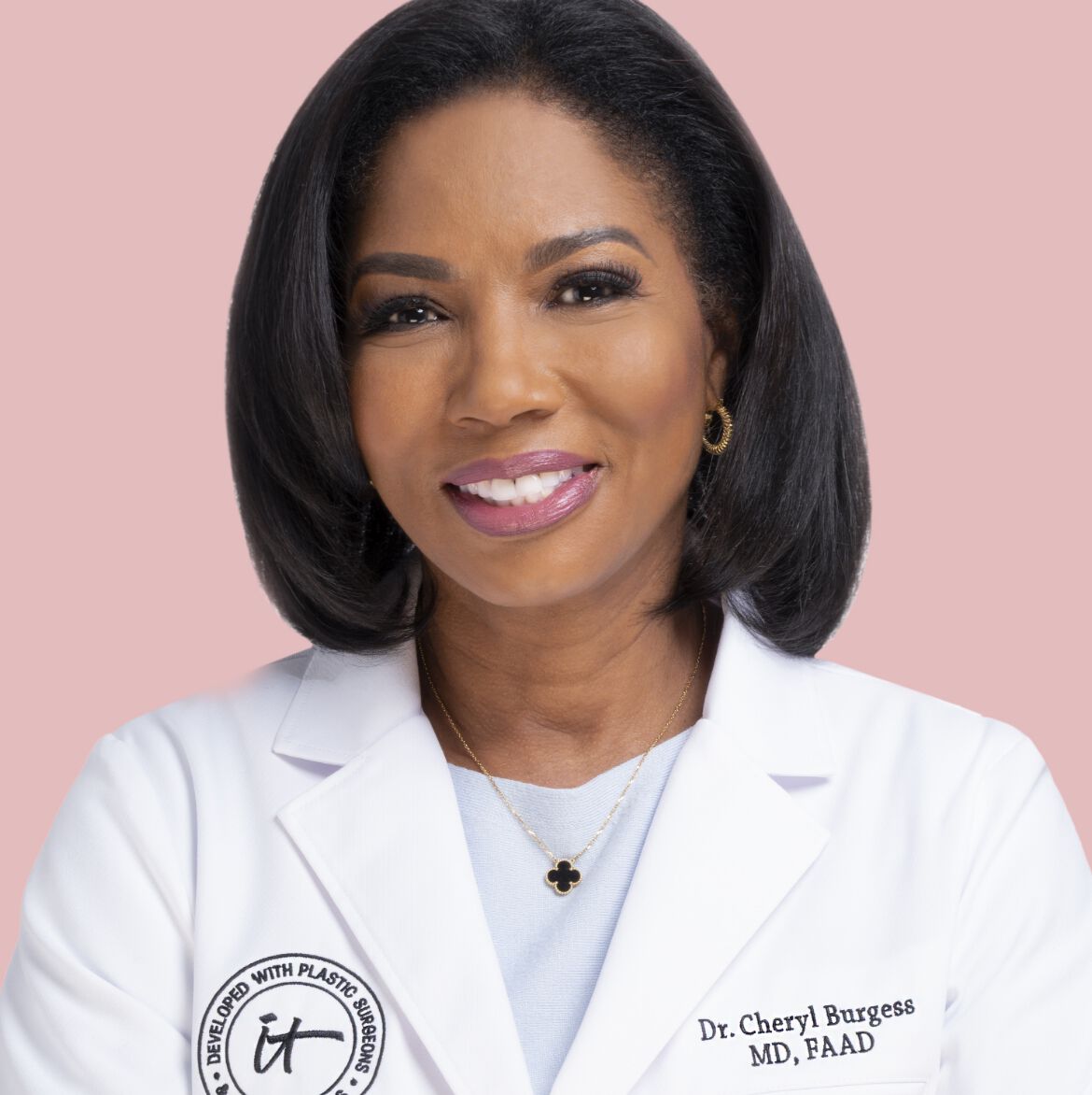 Dr. Cheryl Burgess smiling in a white lab coat with IT Cosmetics badge, posed against a soft pink background.