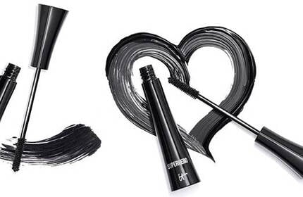 Two open tubes of IT Cosmetics Superhero mascara with black mascara swipes forming a heart shape.