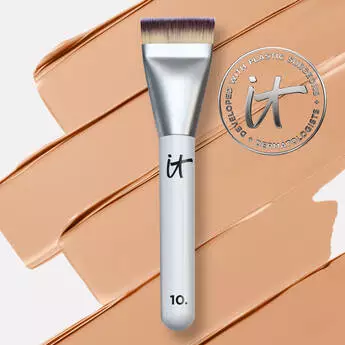 IT Cosmetics makeup brush with flat top bristles placed over tan foundation swatch and brand logo in background.