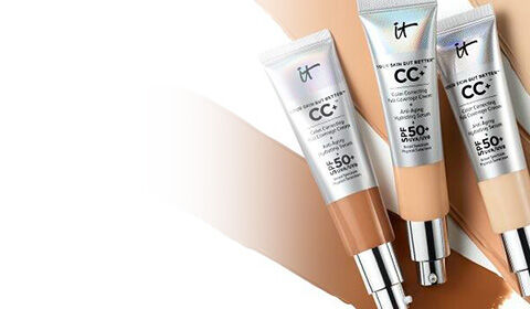 Three tubes of IT Cosmetics CC+ Cream with SPF 50+ placed over tan and beige foundation swatches.