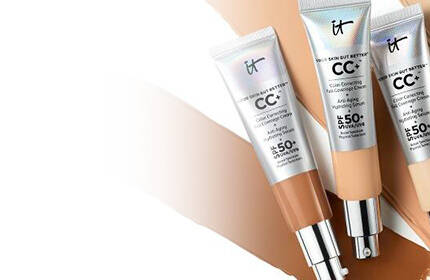 Three tubes of IT Cosmetics CC+ Cream with SPF 50+ placed over tan and beige foundation swatches.