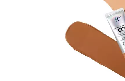 Partial view of IT Cosmetics CC+ Cream tube with deep shade foundation swatch in background.